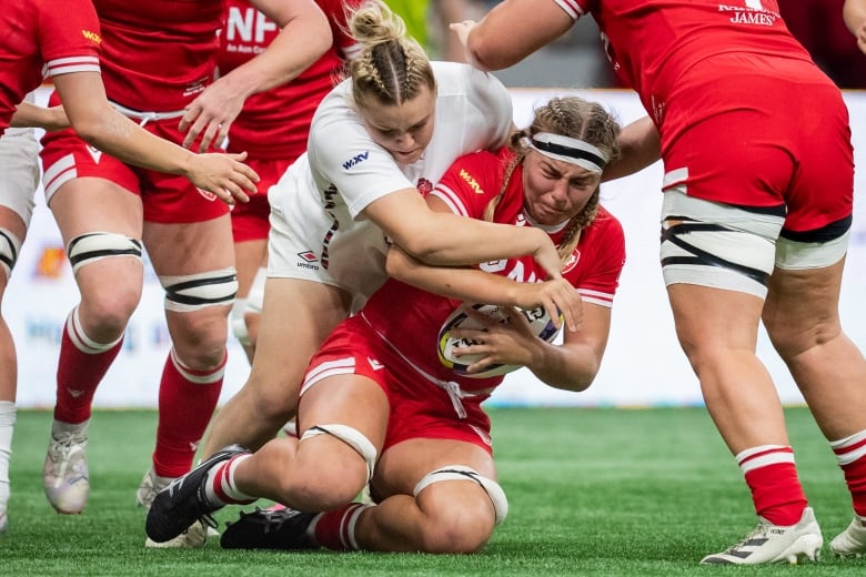 A female rugby union player is dragged down by a defender while holding the ball during a match.