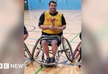 Patrick Murphy, sat in his wheelchair and holding a rugby league trophy in a gymnasium.