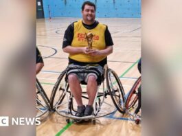 Patrick Murphy, sat in his wheelchair and holding a rugby league trophy in a gymnasium.