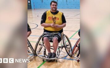 Patrick Murphy, sat in his wheelchair and holding a rugby league trophy in a gymnasium.