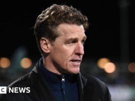 Mullin looking to the side, he has brown hair and is wearing a navy blue zip-up and a black jacket.