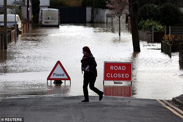 A woman walks next to flooding on a road after Storm Darragh hit the country, in Hereford on Sunday