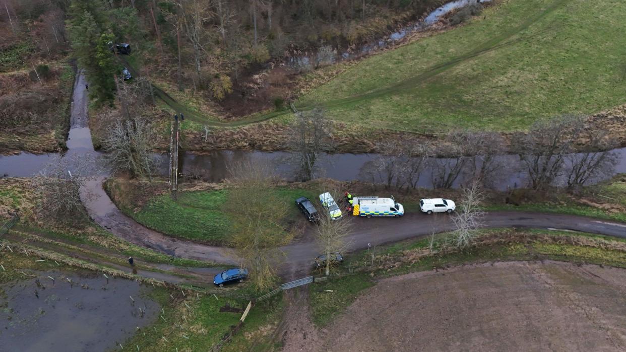 An aerial shot of Abberwick Ford where a very rural road crosses the river Aln. Five vehicles including two police vehicles are parked up.