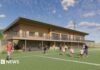 An architect's illustration showing what the new rugby clubhouse would look like. It is a two=-storey building made from wood and has a balcony extending along it. On the pitch are some children being coached, some people standing on the sidelines and a man running.