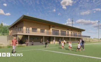 An architect's illustration showing what the new rugby clubhouse would look like. It is a two=-storey building made from wood and has a balcony extending along it. On the pitch are some children being coached, some people standing on the sidelines and a man running.
