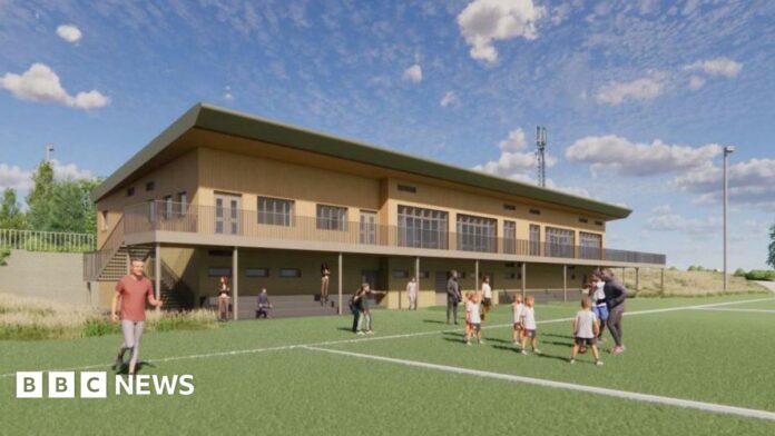 An architect's illustration showing what the new rugby clubhouse would look like. It is a two=-storey building made from wood and has a balcony extending along it. On the pitch are some children being coached, some people standing on the sidelines and a man running.