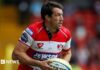 Tom Voyce playing for Gloucester, wearing a red and white shirt and carrying a ball.