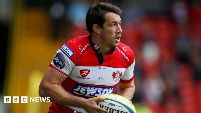 Tom Voyce playing for Gloucester, wearing a red and white shirt and carrying a ball.