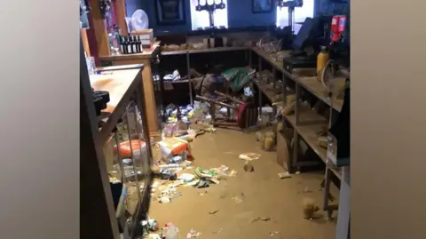 BBOB Rugby Club Flood waters in a bar with bottles and crisp packets floating in the brown water.