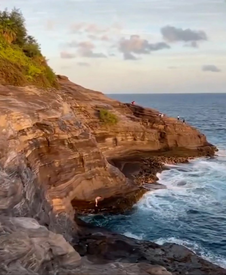 Person jumping from a cliff into the ocean in Hawaii.