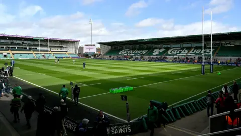 Getty Images A photo from a corner of a rugby stadium. The sun and sky are clear and the pitch is bright green. There are two empty stands overlooking the pitch.