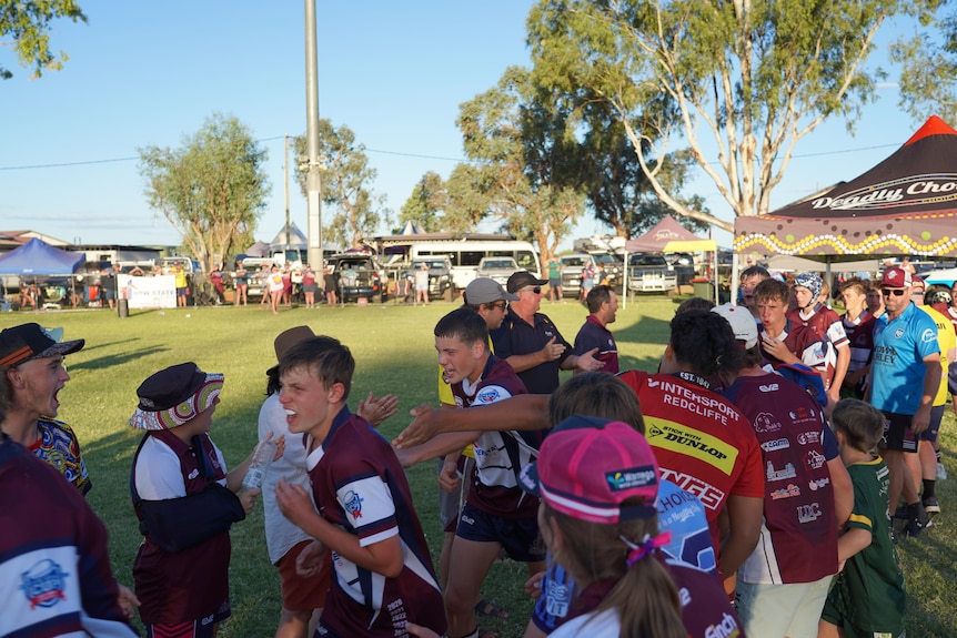 Boys on a junior rugby league team run past spectators on the side of an oval.