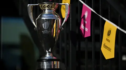 Getty Images A photo of a shiny silver trophy. In the background there are pink and yellow bunting to represent the women's rugby world cup