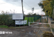 A gate road leading past a field to a rugby club