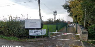 A gate road leading past a field to a rugby club