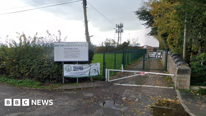 A gate road leading past a field to a rugby club