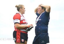 Mackenzie Carson on the left, wearing a black, white and red uniform. She is facing her partner Sarah Bern, who is wearing a blue uniform.