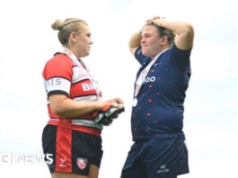 Mackenzie Carson on the left, wearing a black, white and red uniform. She is facing her partner Sarah Bern, who is wearing a blue uniform.