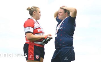 Mackenzie Carson on the left, wearing a black, white and red uniform. She is facing her partner Sarah Bern, who is wearing a blue uniform.